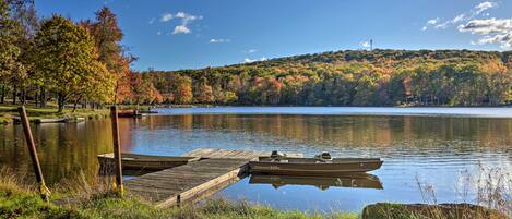 Un lac paisible où sont amarrés des bateaux, entouré d’arbres aux feuilles d’automne, et un ciel dégagé.