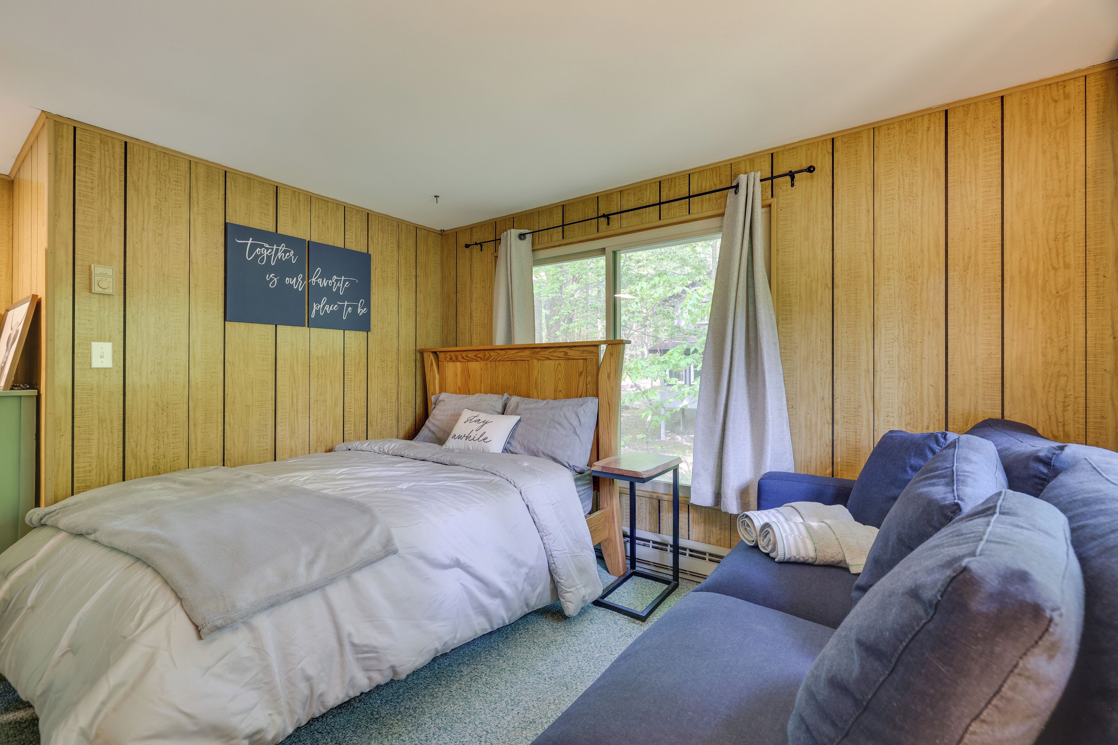 Una camera da letto con un letto, un tavolino, una poltrona, pareti in legno, una finestra con tende e decorazioni motivazionali al muro.