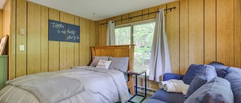 Una camera da letto con un letto, un tavolino, una poltrona, pareti in legno, una finestra con tende e decorazioni motivazionali al muro.