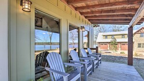 A covered porch with Adirondack chairs, a wooden deck, and a view of a lake and buildings in the background. - Shoreline Home w/ Boat Dock & Fire Pit in Shelby! (Shelby)