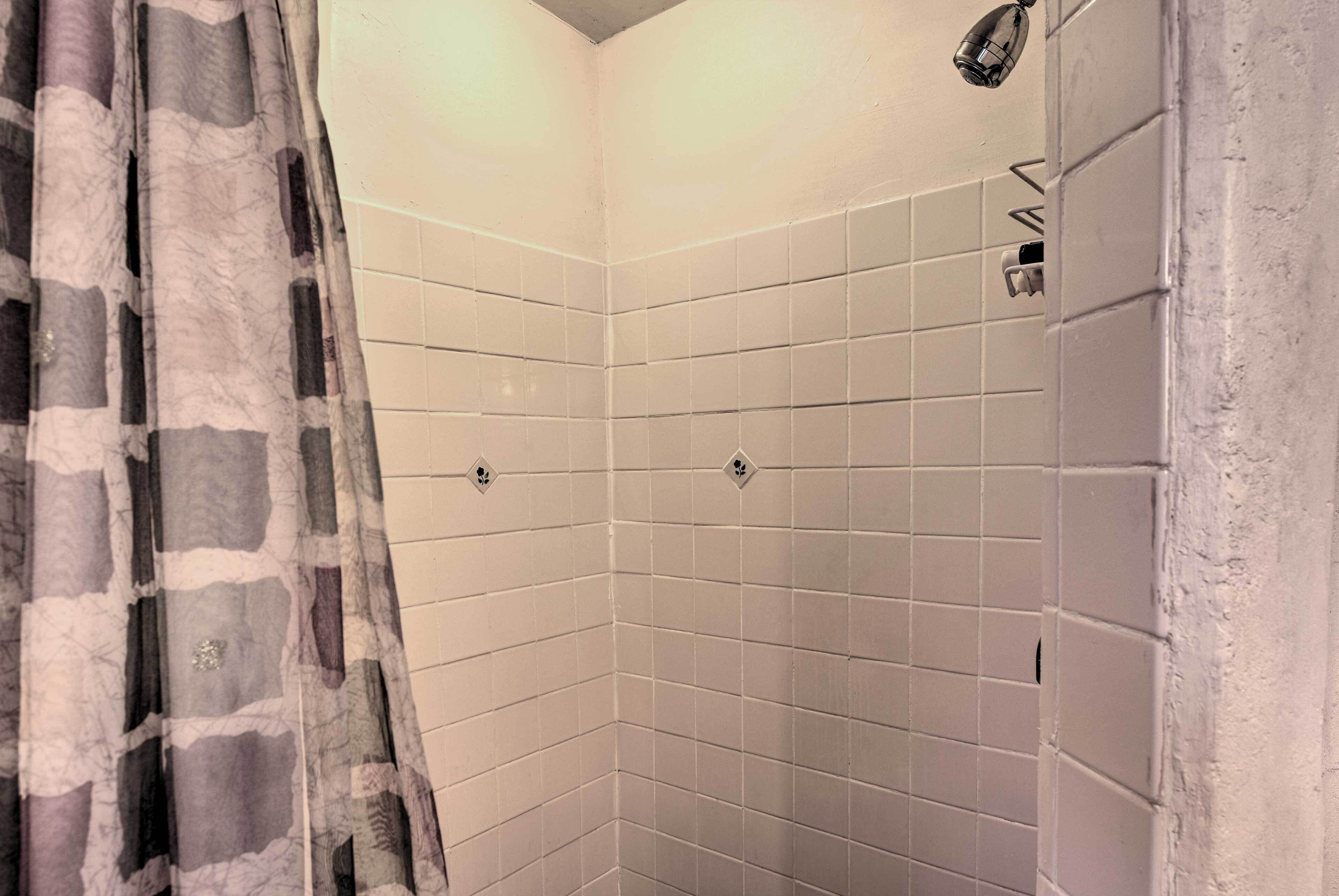 A corner shower with white tiles and a patterned curtain.