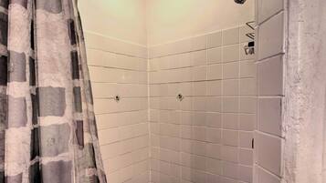 A corner shower with white tiles and a patterned curtain.