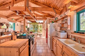 Une cuisine en bois équipée d’une cuisinière, d’un évier et d’un réfrigérateur. On y trouve des placards en bois et une fenêtre.