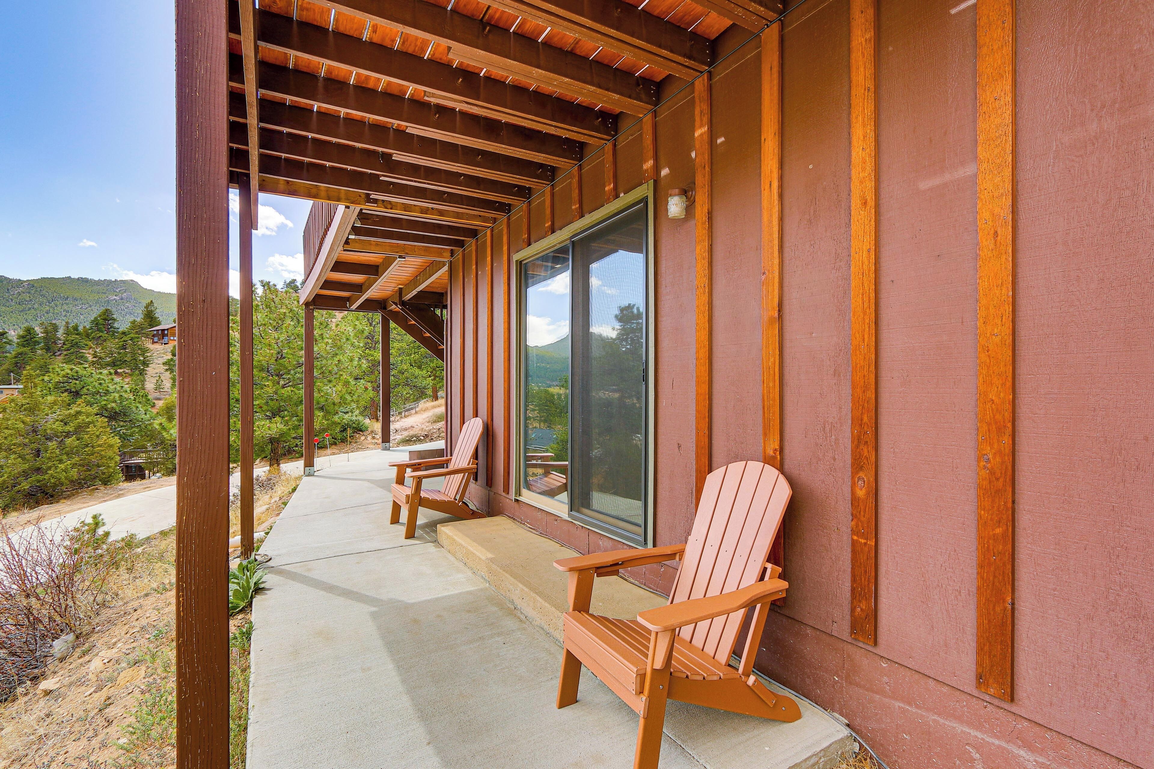 A covered porch with wooden chairs, a large window, and a view of a mountainous landscape.