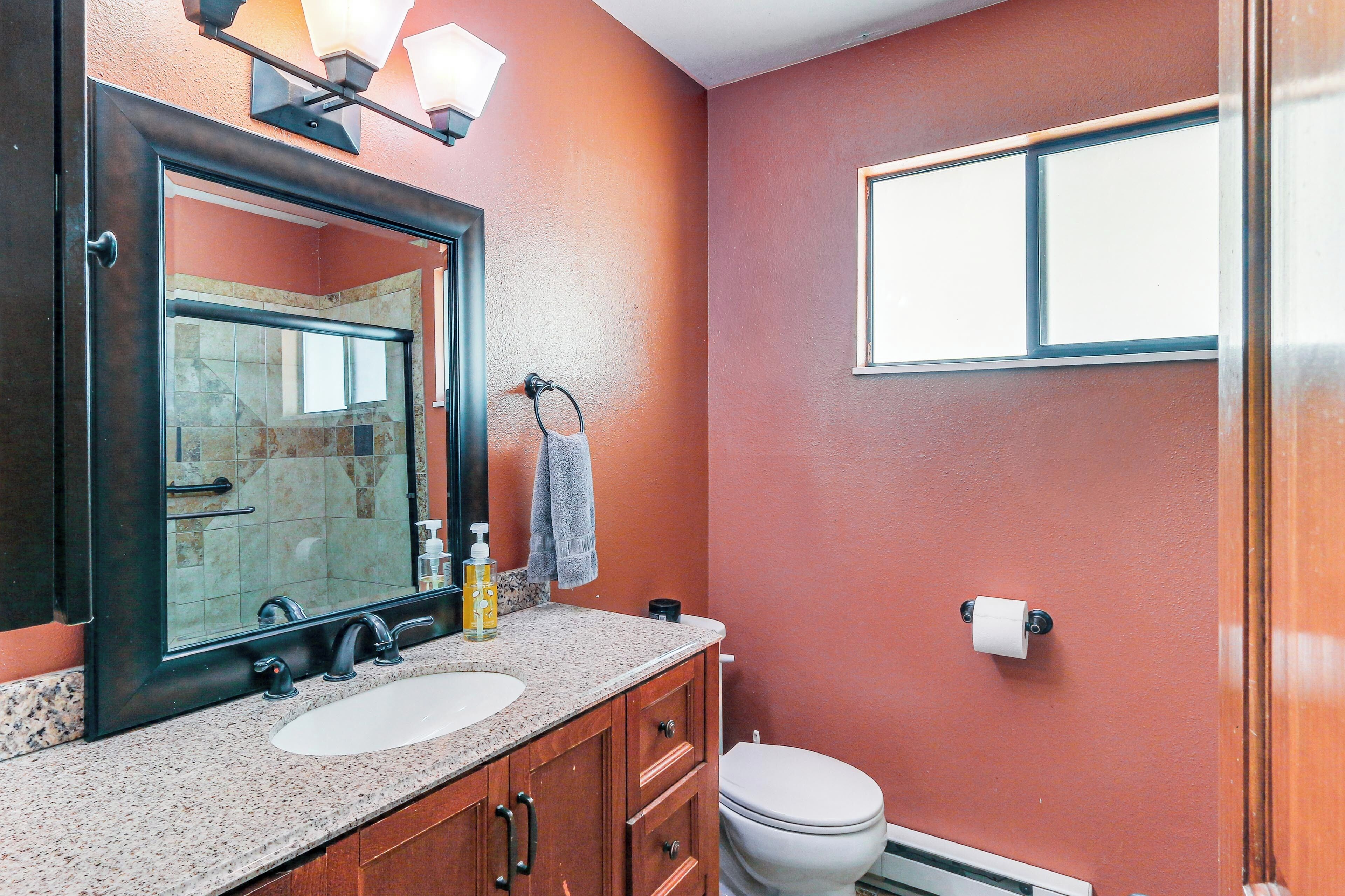 Ein Badezimmer mit Waschbecken, Spiegel, Handtuchhalter, Toilette und einem Fenster.