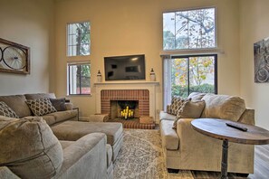 A living room with a fireplace, sofas, a TV, and large windows. - Well-appointed Condo Across Street From UC Davis! (Davis)