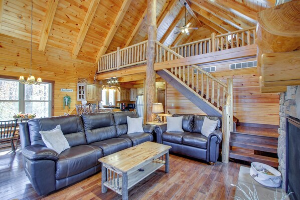 En rummelig opholdsstue med en stor lædersofa, et træbord og en trappe til en etage ovenover.