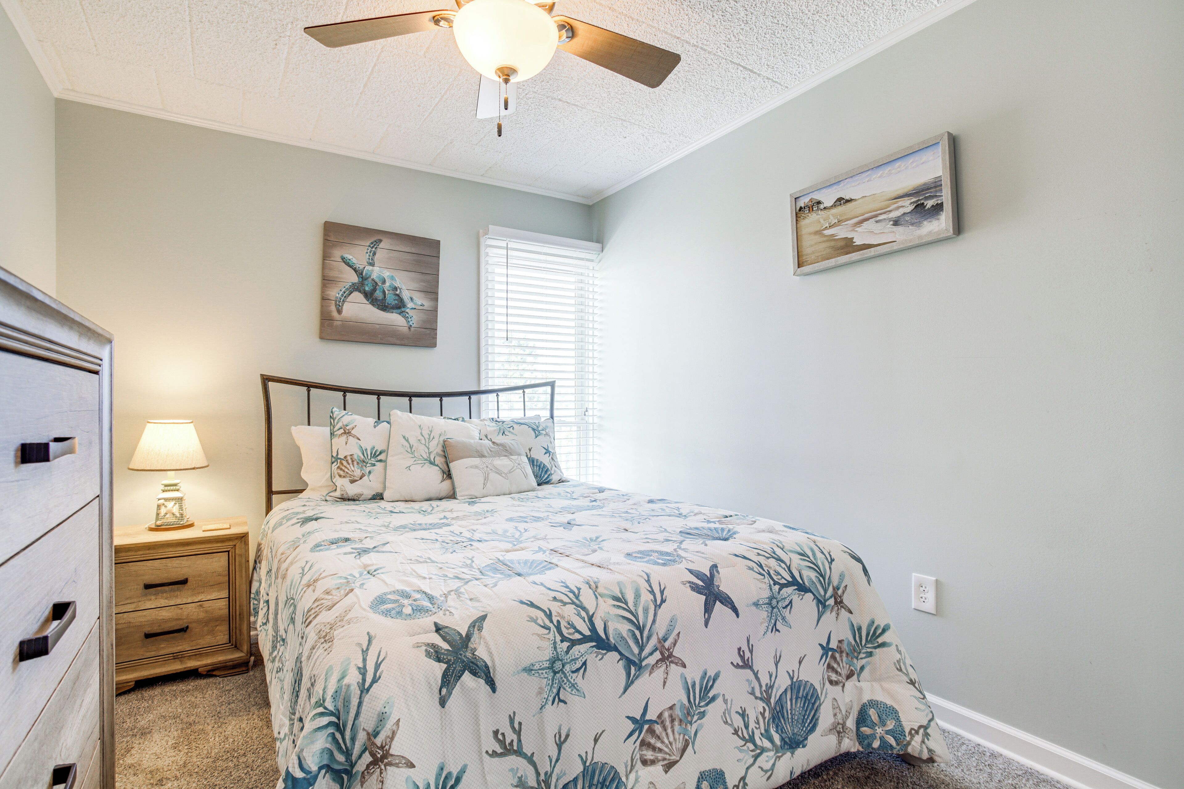 A bedroom with a bed, a nightstand, a ceiling fan, and artwork on the walls.