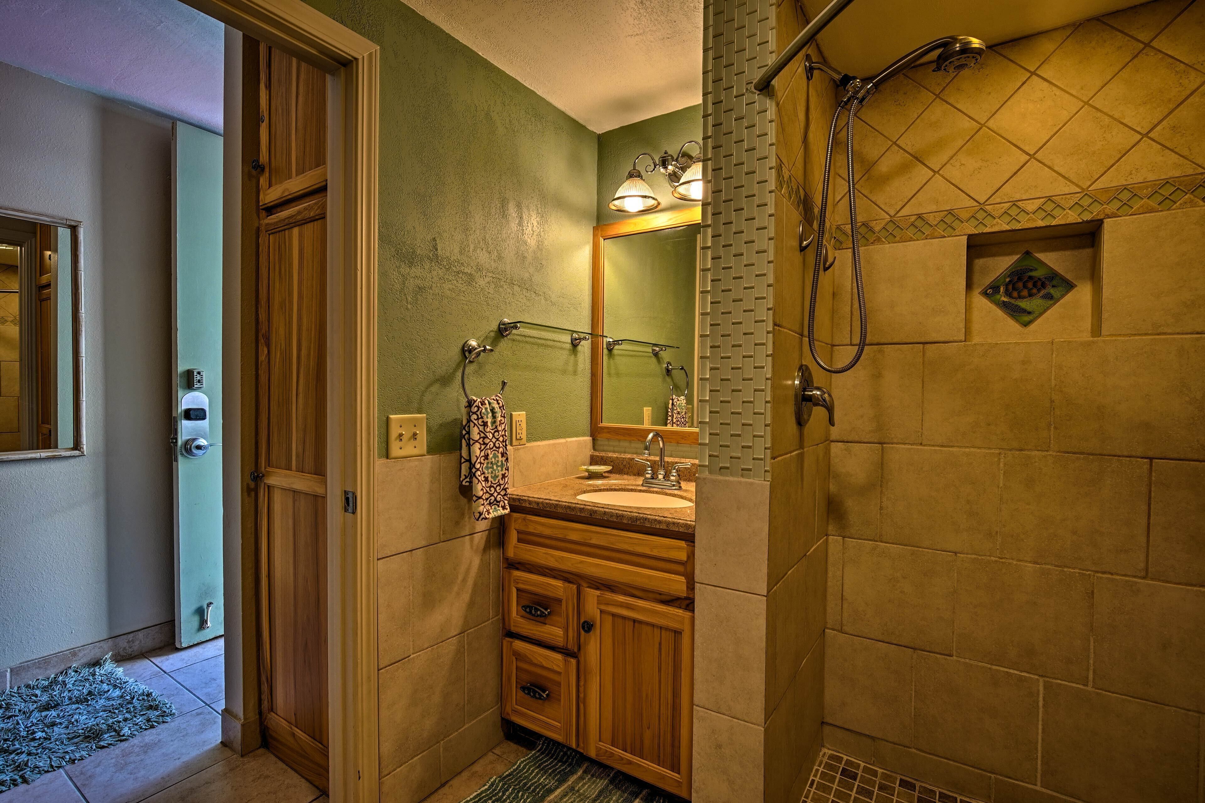 A bathroom with a wooden vanity, a sink, a mirror, and a shower area.