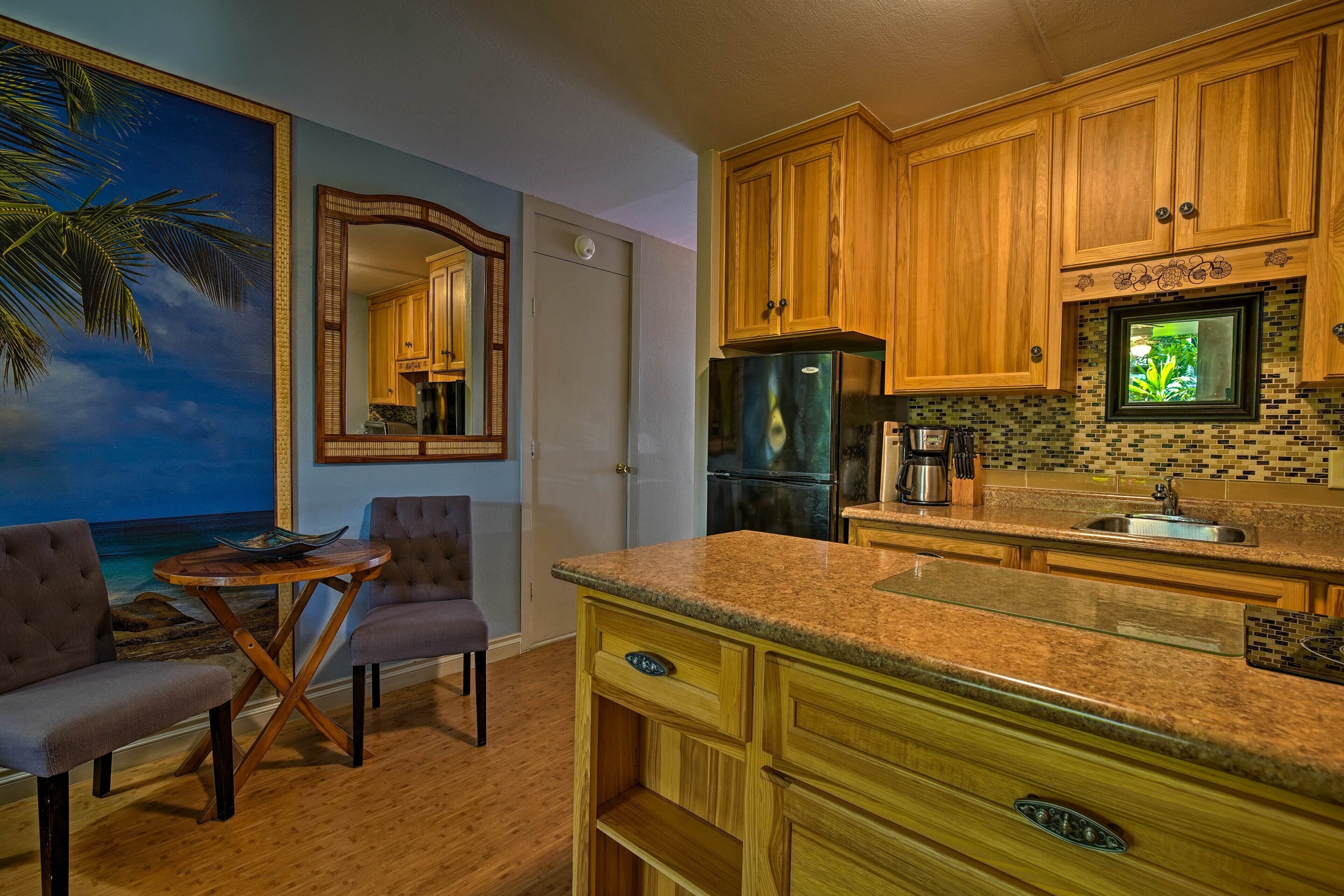 A kitchen with wooden cabinets, a granite countertop, and a view of a palm tree through a window.