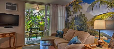 Un salón con sofá, mesa de centro, televisor y un mural de paisaje tropical.