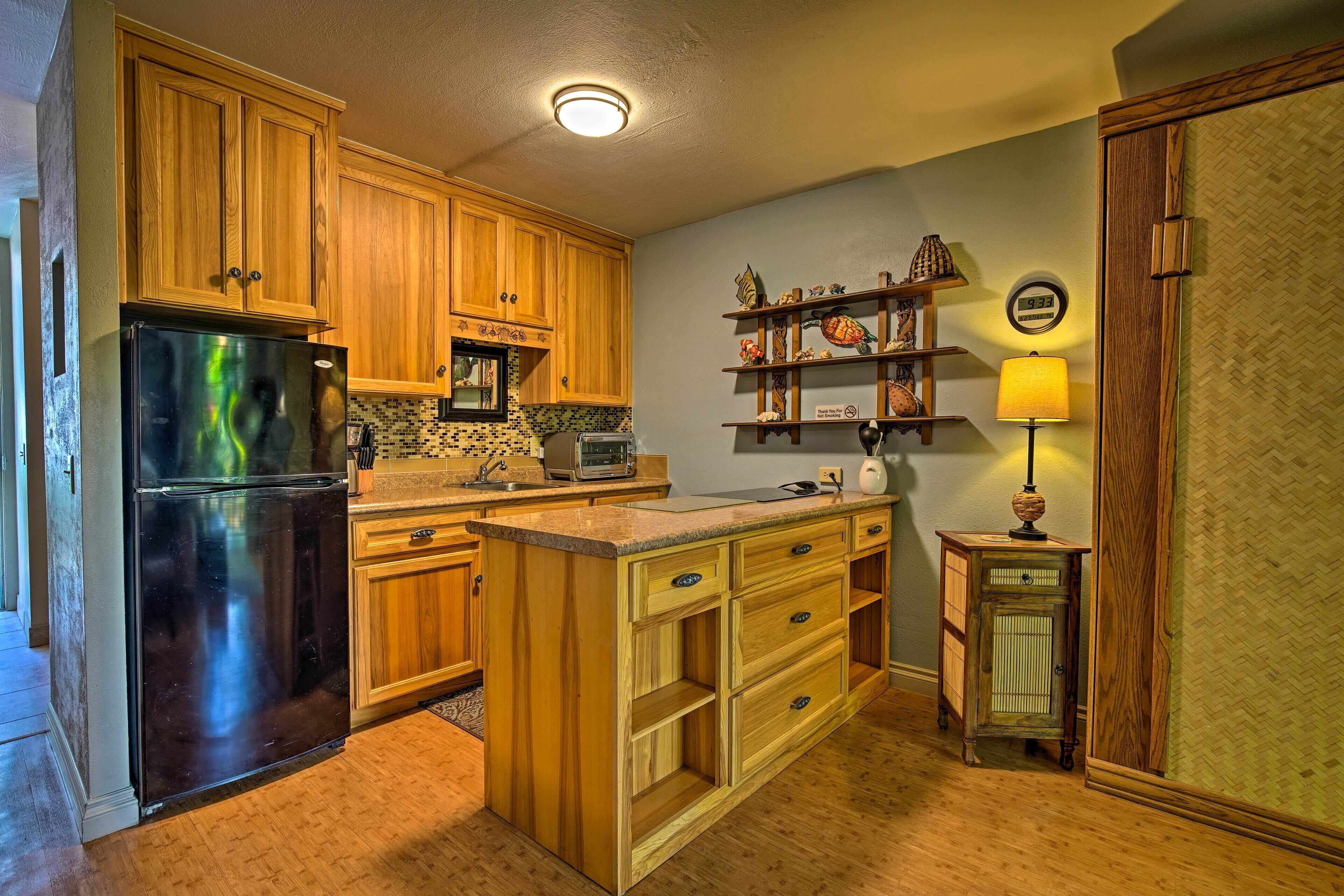 A kitchen with wooden cabinets, a black refrigerator, a microwave, and a toaster. There is a small shelf with decorative items and a clock on the wall.