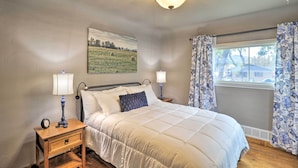 A bedroom with a bed, nightstands, lamps, a painting, and a window with curtains. - Comfy & Cozy Kalispell Home: Walk to Downtown (Kalispell)