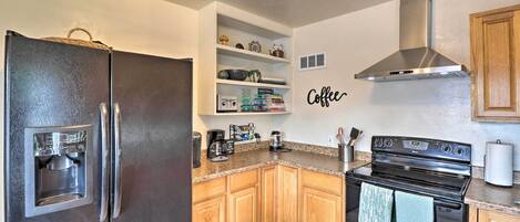 A kitchen with a stainless steel refrigerator, wooden cabinets, a built-in oven, and a coffee-themed wall decoration.