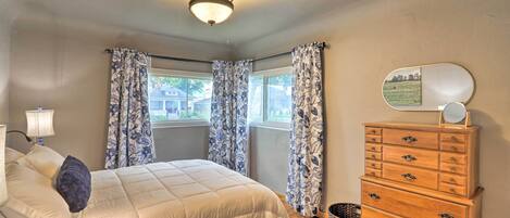 A bedroom with a bed, dresser, and windows with curtains.