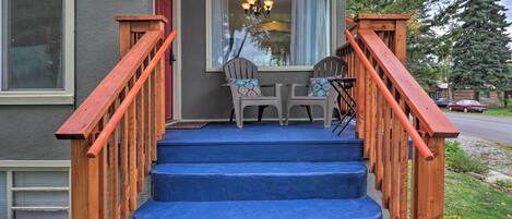 Eine Holztreppe mit blauen Stufen führt zu einem Laube mit zwei Adirondack-Stühlen und einer Chandelier.