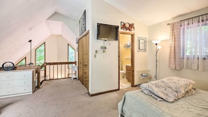 Une chambre à coucher comprenant un lit, une commode, un téléviseur fixé au mur et une porte donnant accès à une salle de bain.