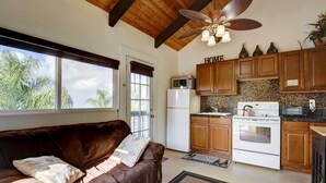 A cozy living room with a brown leather sofa and a view of the kitchen. - Cozy Kona Coast Apt w/ Lanai ~ 8 Miles to Beach! (Kailua-Kona)