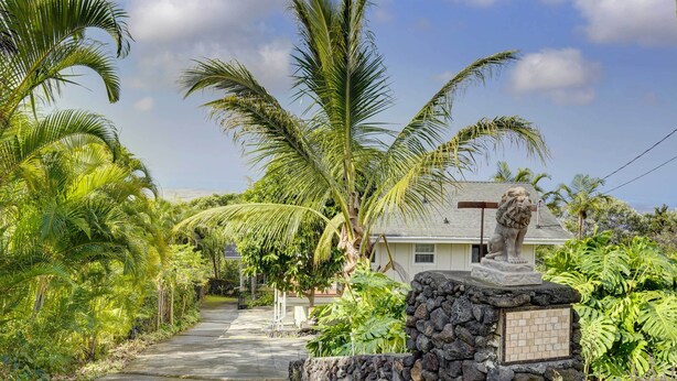 A pathway lined with palm trees leading to a house with a lion statue in front. - Cozy Kona Coast Apt w/ Lanai ~ 8 Miles to Beach! (Kailua-Kona)