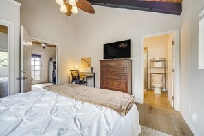 A bedroom with a bed, a desk, a television, and a bathroom visible through an open door. - Cozy Kona Coast Apt w/ Lanai ~ 8 Miles to Beach! (Kailua-Kona)