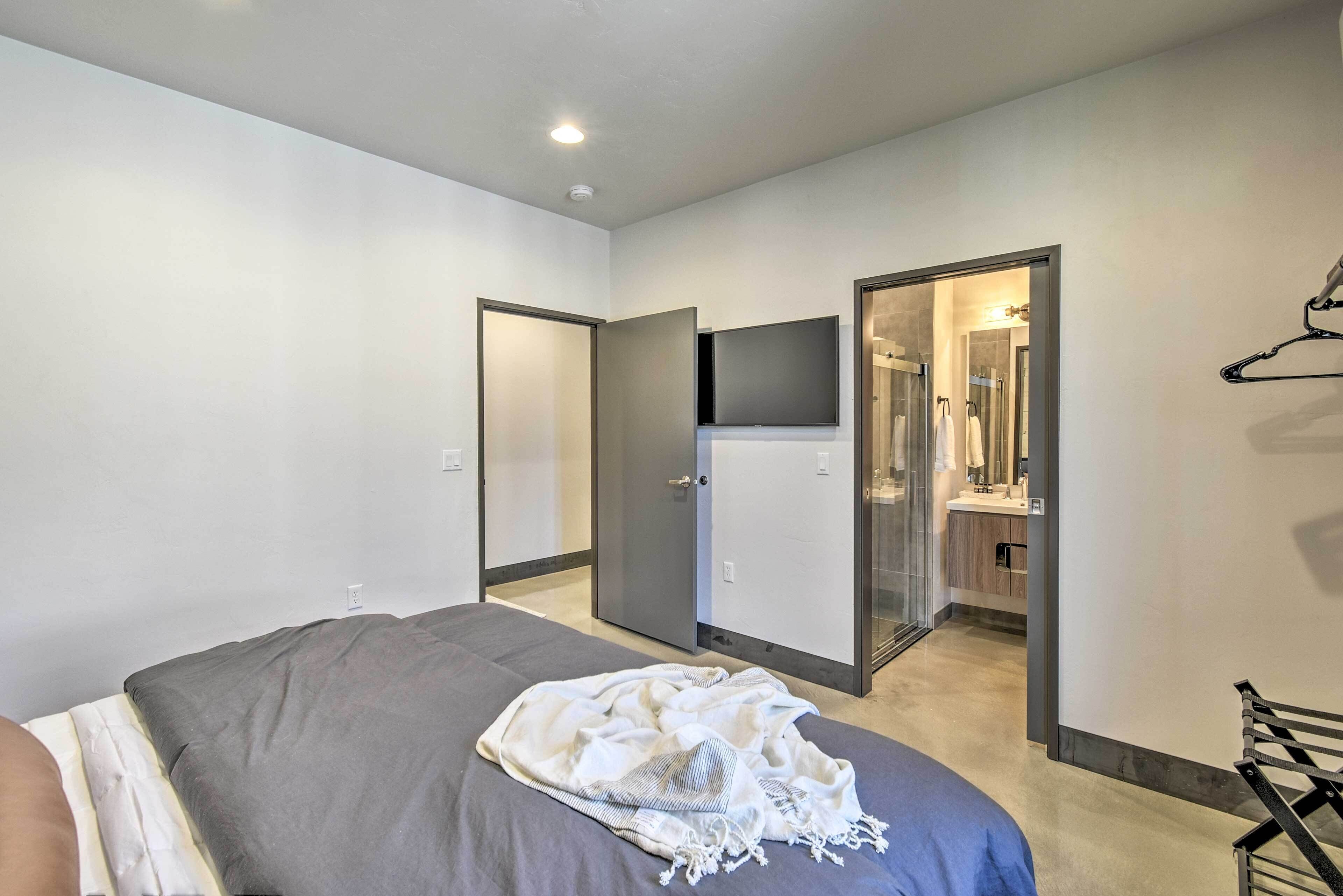 A bedroom with a bed, a bedside table, a TV, and a bathroom visible through an open door.