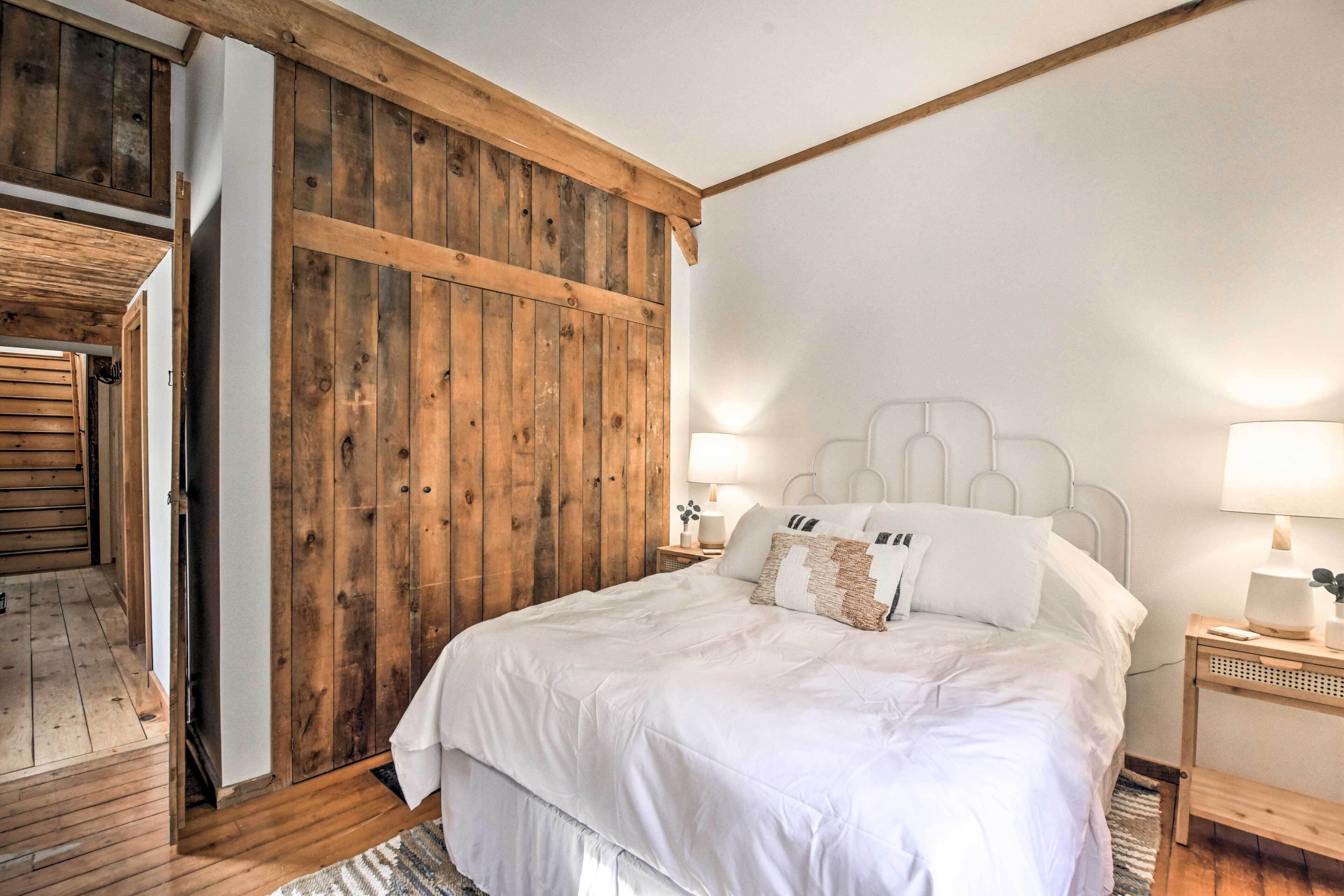 Un dormitorio con un armario de madera, una cama con ropa de cama blanca, dos lámparas de noche y una mesita de noche con lámpara.