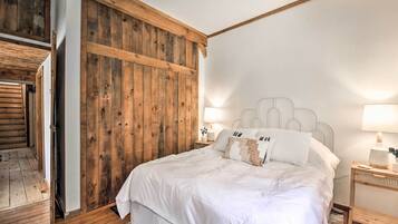 Un dormitorio con un armario de madera, una cama con ropa de cama blanca, dos lámparas de noche y una mesita de noche con lámpara.