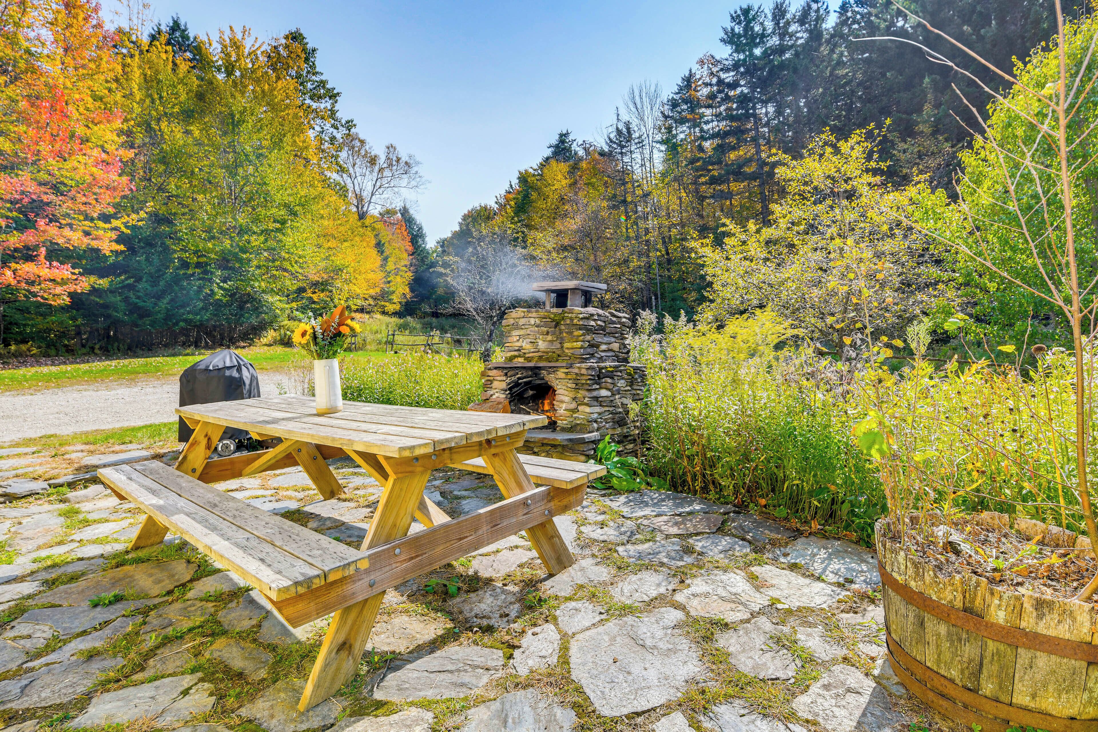 A stone fireplace with a chimney, surrounded by a stone wall and a wooden bench.