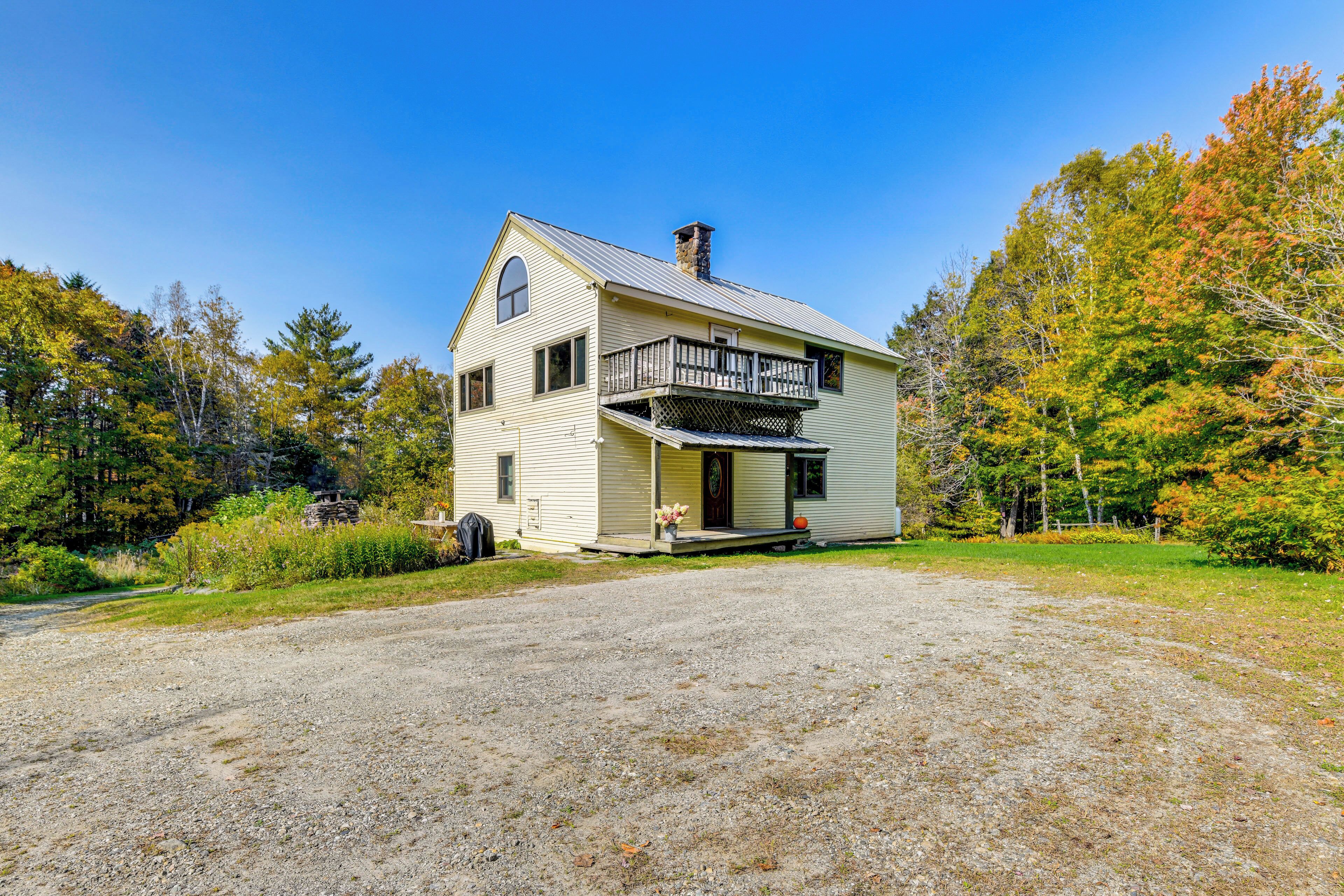A two-story house with a front porch, a chimney, and a gravel driveway.