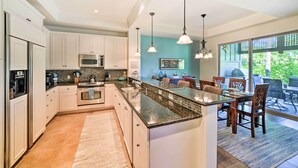 A modern kitchen with white cabinets, stainless steel appliances, a granite countertop, and pendant lighting. - Kona Coast Condo w/ Lanai & Outdoor Kitchen! (Kamuela)