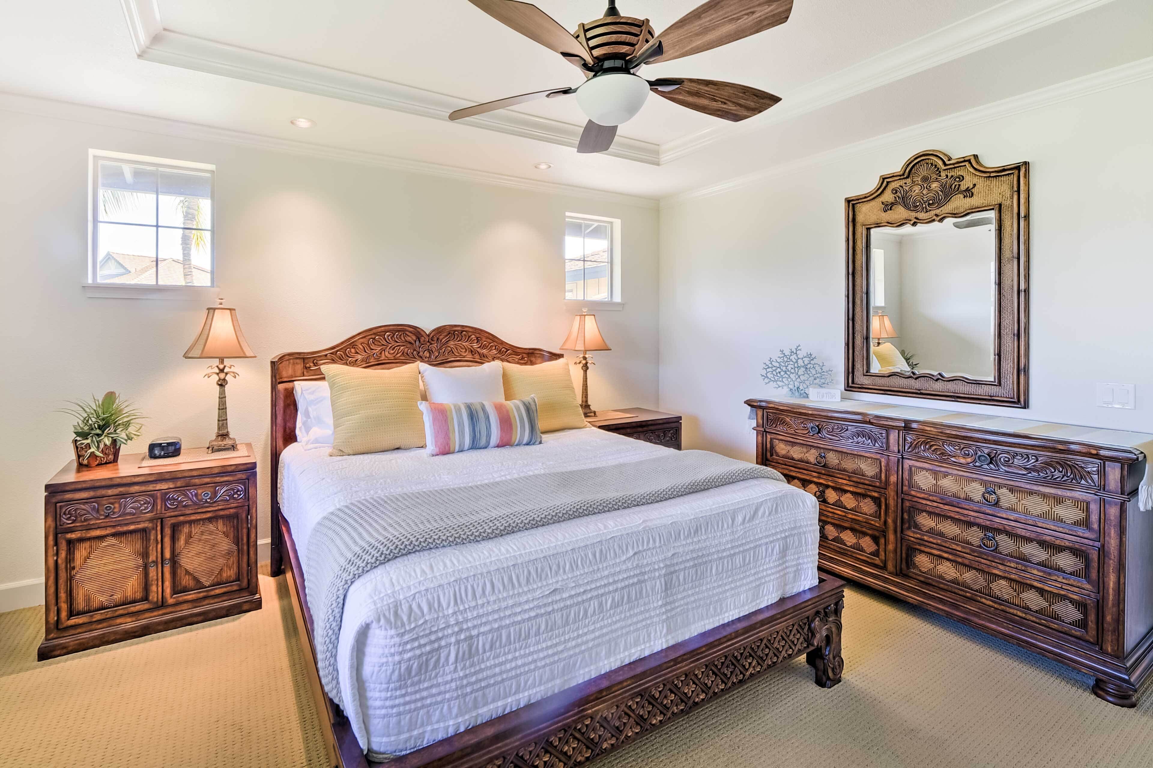 A bedroom with a large bed, wooden nightstands, a dresser, a ceiling fan, and two windows.