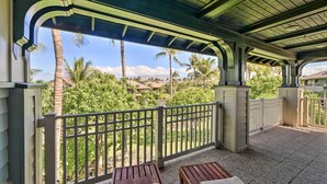 A covered outdoor area with two wooden benches and a metal railing, overlooking a lush garden with palm trees and a clear sky. - Kona Coast Condo w/ Lanai & Outdoor Kitchen! (Kamuela)