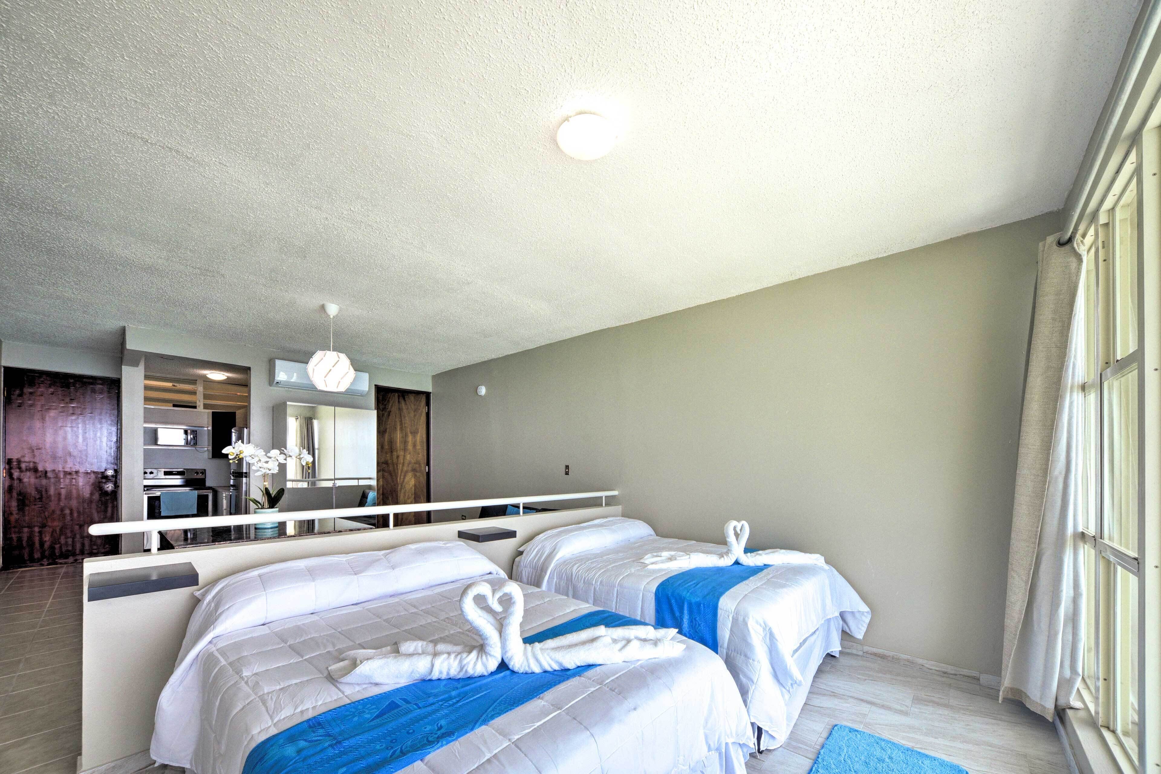 A hotel room with two beds, a kitchenette, and a bathroom.