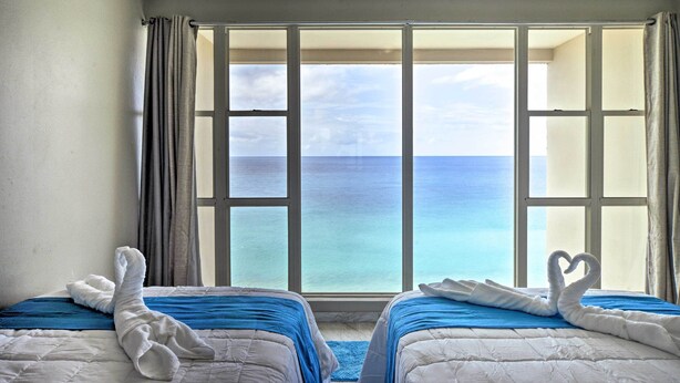 Une chambre d’hôtel avec deux lits, une grande fenêtre donnant sur la mer et des serviettes disposées sur les lits.