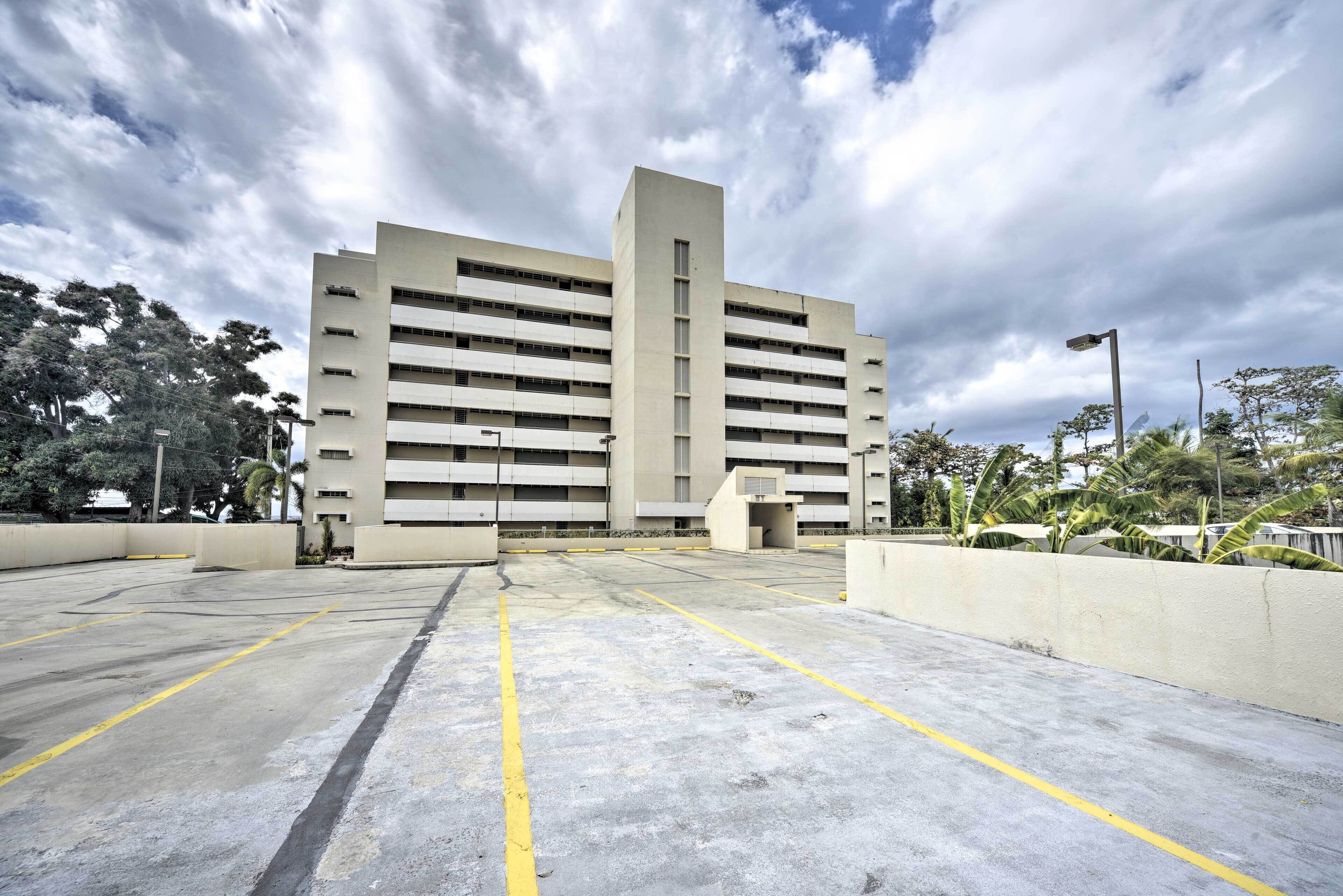 A multi-story parking garage with a central vertical structure, surrounded by trees and a cloudy sky.