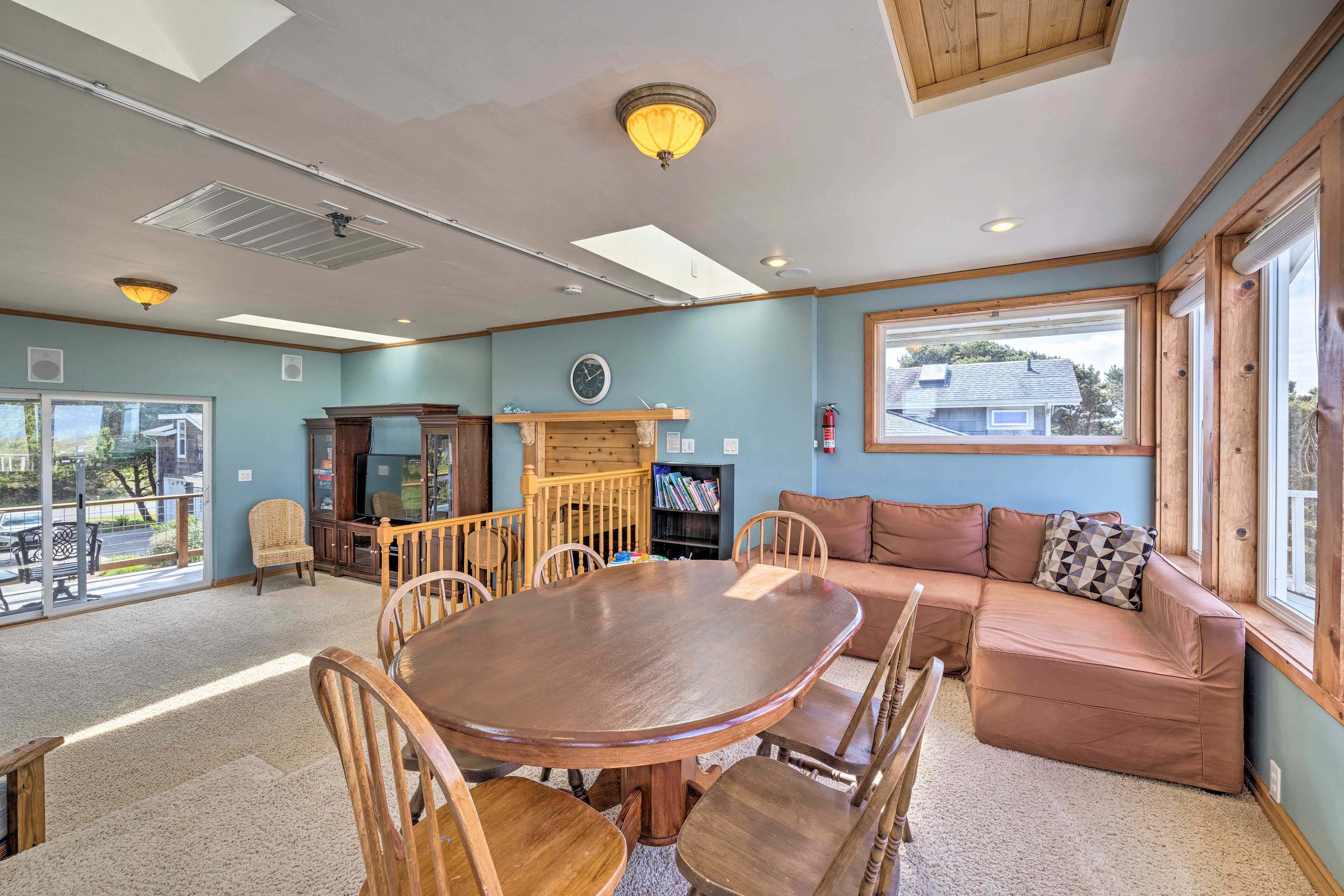 A spacious living room with a wooden dining table, comfortable seating, a fireplace, and large windows offering a view of the outside.