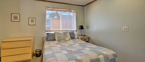 A bedroom with a bed, a dresser, a nightstand, and a window with blinds.
