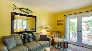 A living room with a sofa, armchair, and a glass coffee table. There is a large mirror, a lamp, and a fish decoration on the wall. - West Palm Beach Home w/ Fenced-in Yard & Deck! (West Palm Beach)