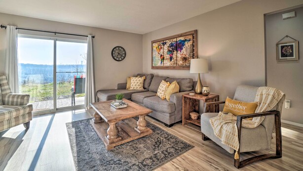 A living room with a sofa, armchair, coffee table, and a view through a sliding glass door. - Sunny Family-friendly Branson Home! (Branson)