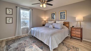 A bedroom with a bed, a ceiling fan, a nightstand, and a window with curtains. - Sunny Family-friendly Branson Home! (Branson)