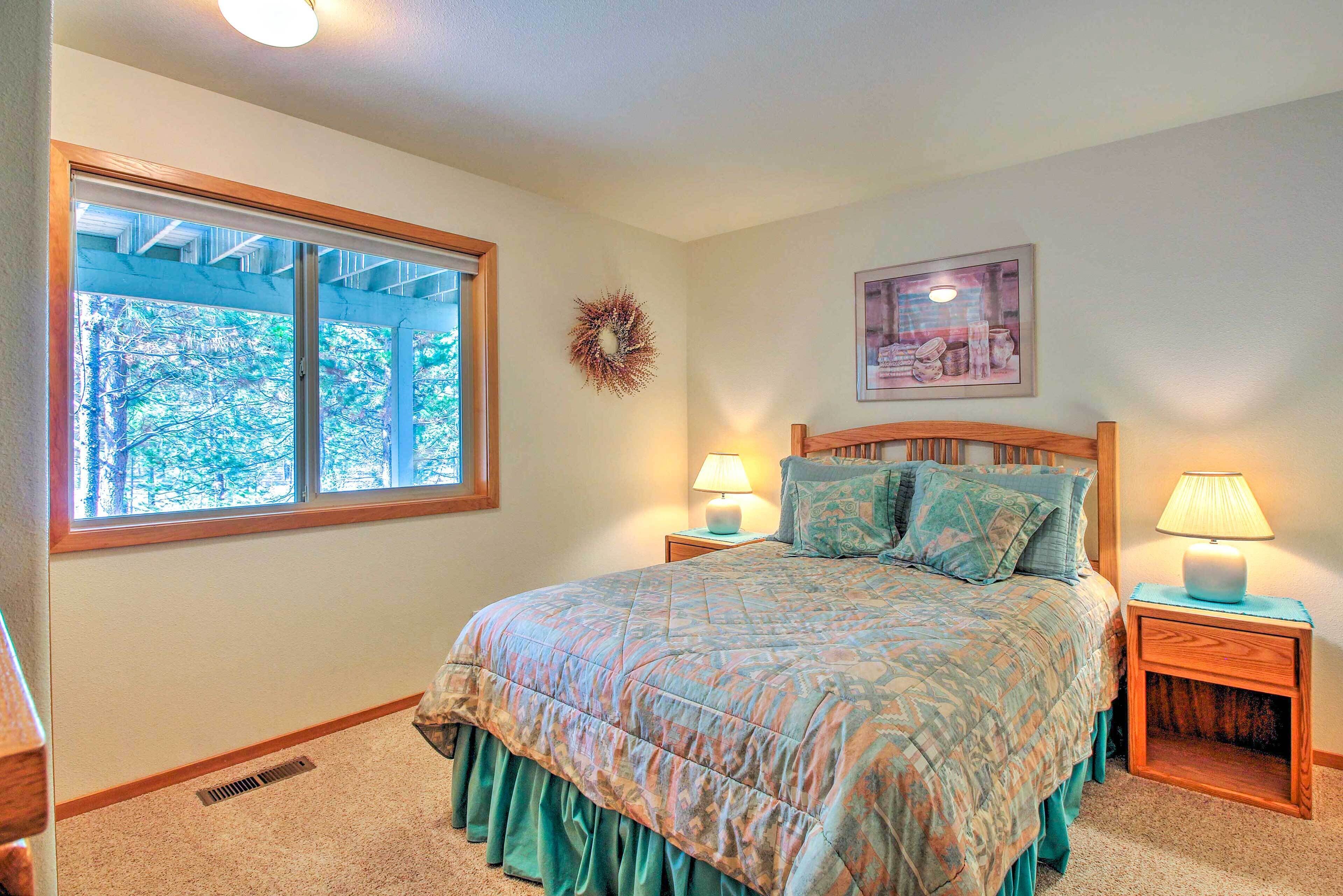 A bedroom with a large bed, two bedside tables with lamps, a window with a view of trees, and a framed picture on the wall.
