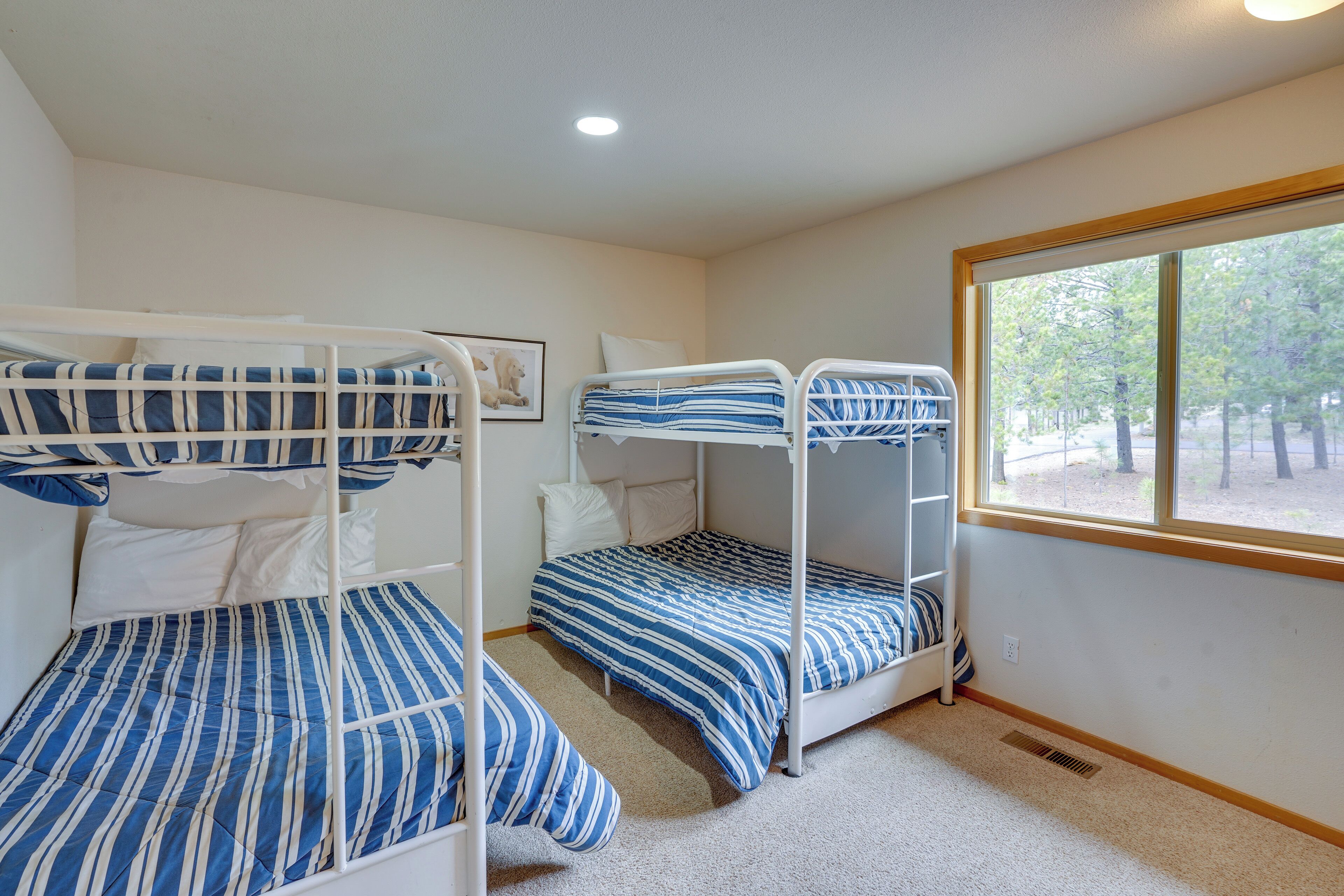 A room with three bunk beds, a window with a view of trees, and a ceiling light.