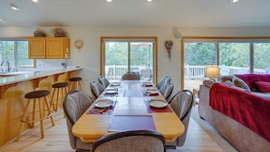 A dining area with a long table set for six, wooden chairs, and a kitchen area with bar stools. - Sunriver Getaway w/ Sharc Waterpark Passes! (Bend)