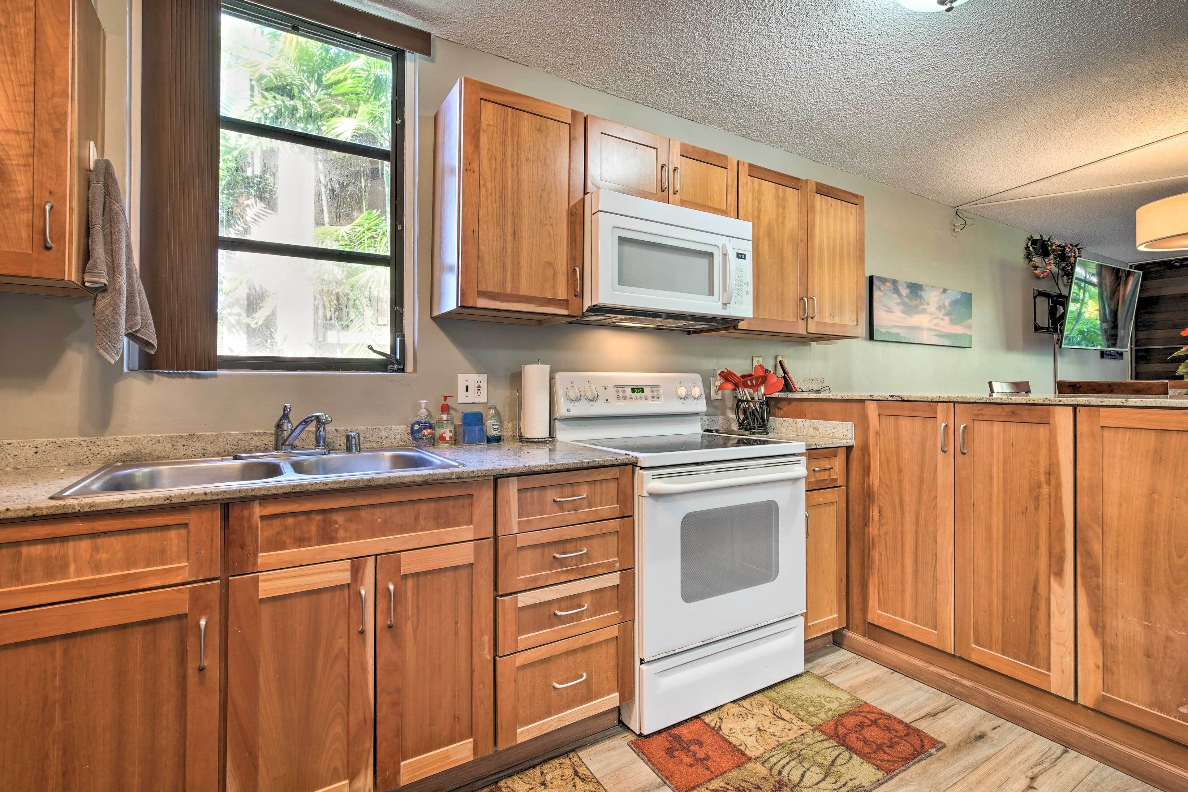 A kitchen with wooden cabinets, a white stove, a microwave, and a sink.