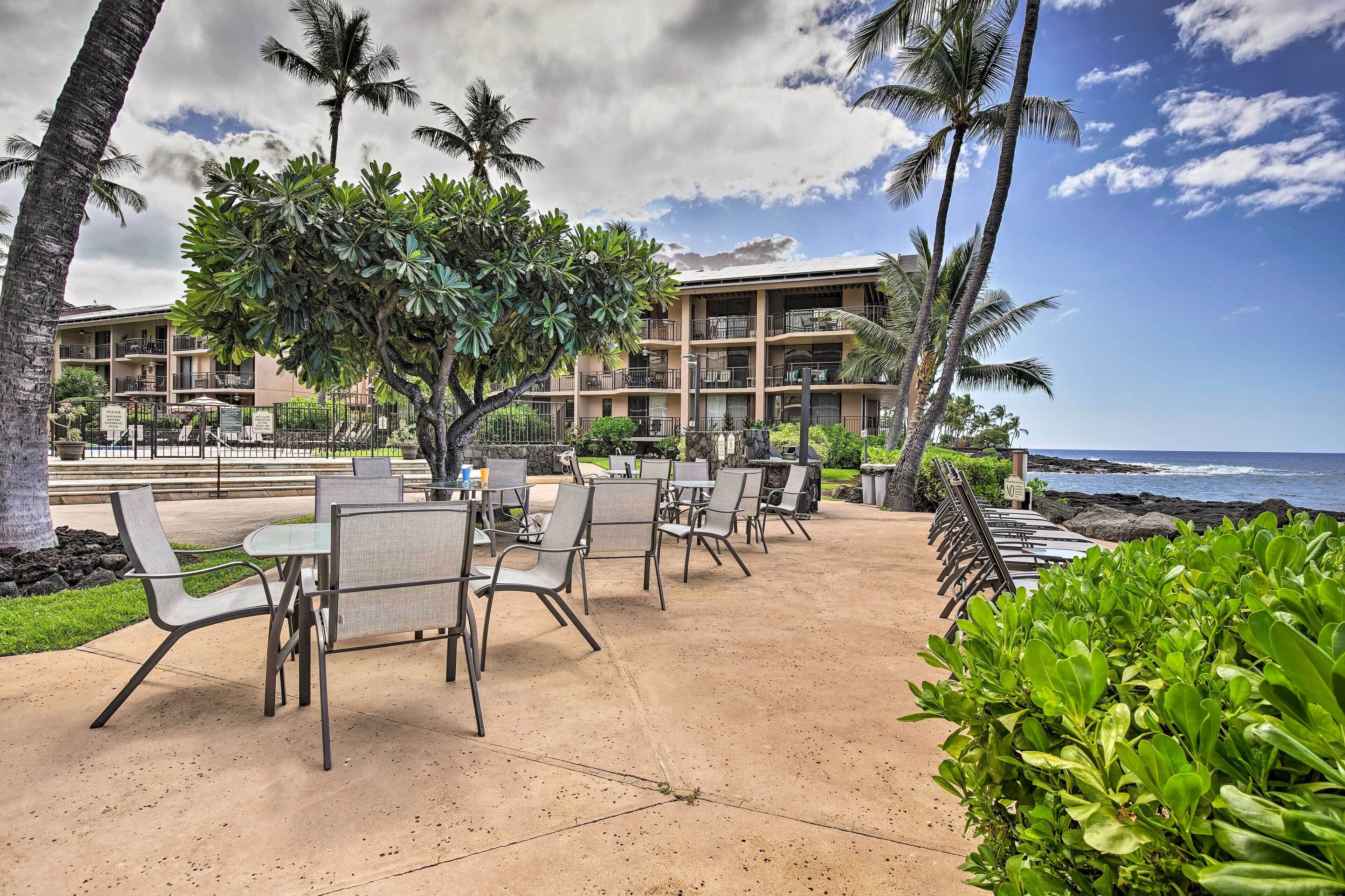 A resort with outdoor seating, palm trees, and a view of the ocean.