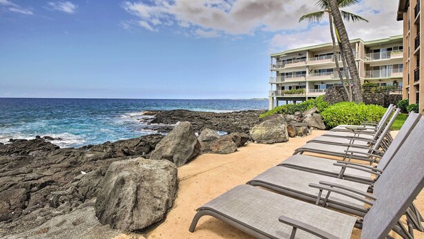 A beachfront hotel with lounge chairs facing the ocean, a rocky shoreline, and a multi-story building with balconies. - Kailua-kona Condo w/ 2 Private Lanais! (Kailua-Kona)