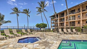 A pool area with lounge chairs and a building with balconies overlooking the ocean. - Kailua-kona Condo w/ 2 Private Lanais! (Kailua-Kona)