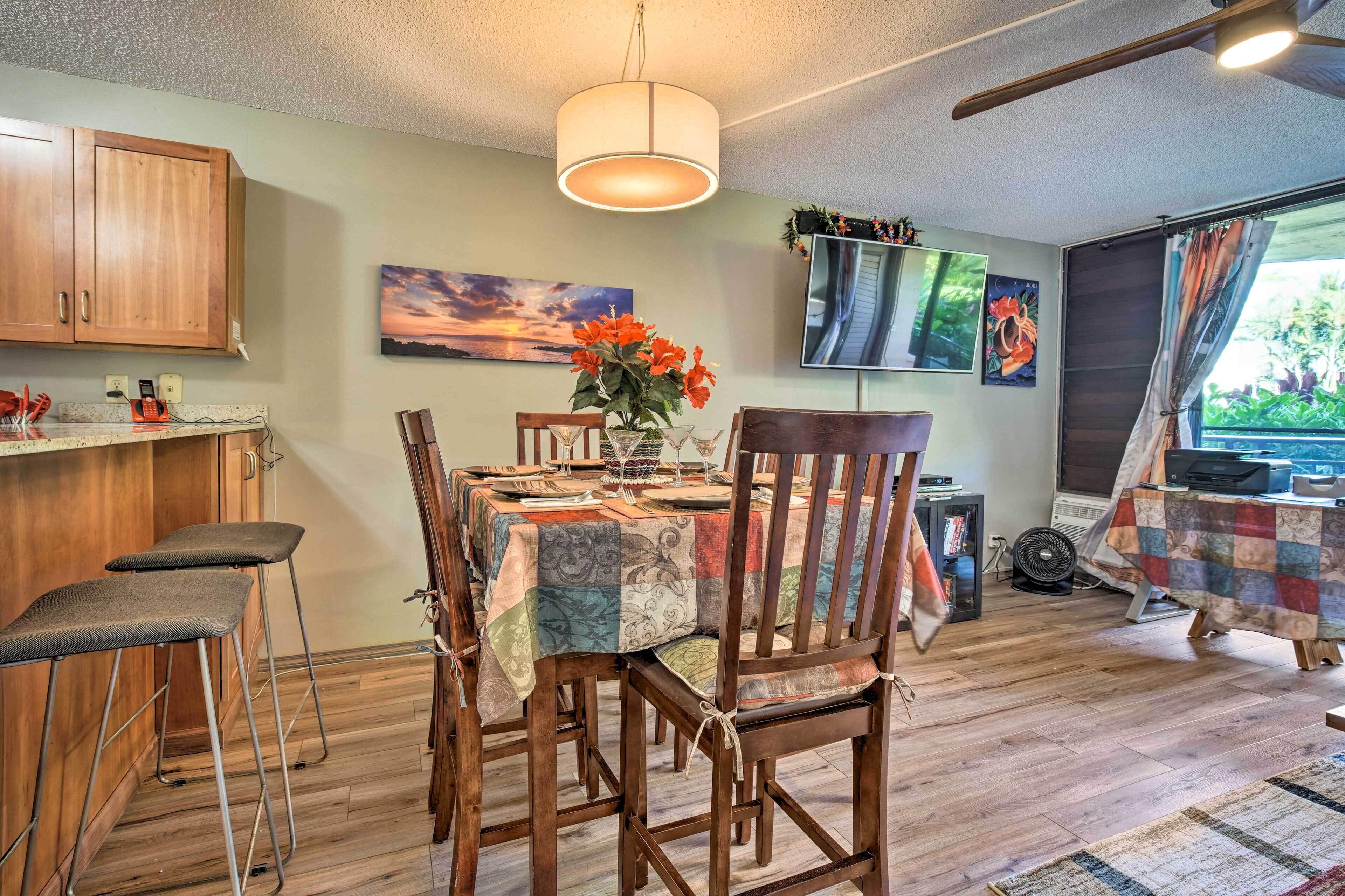 A dining area with a table set for four, wooden chairs, a hanging light fixture, and a painting on the wall.