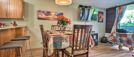 Un coin repas avec une table dressée pour quatre personnes, des chaises en bois, un luminaire suspendu et un tableau accroché au mur.