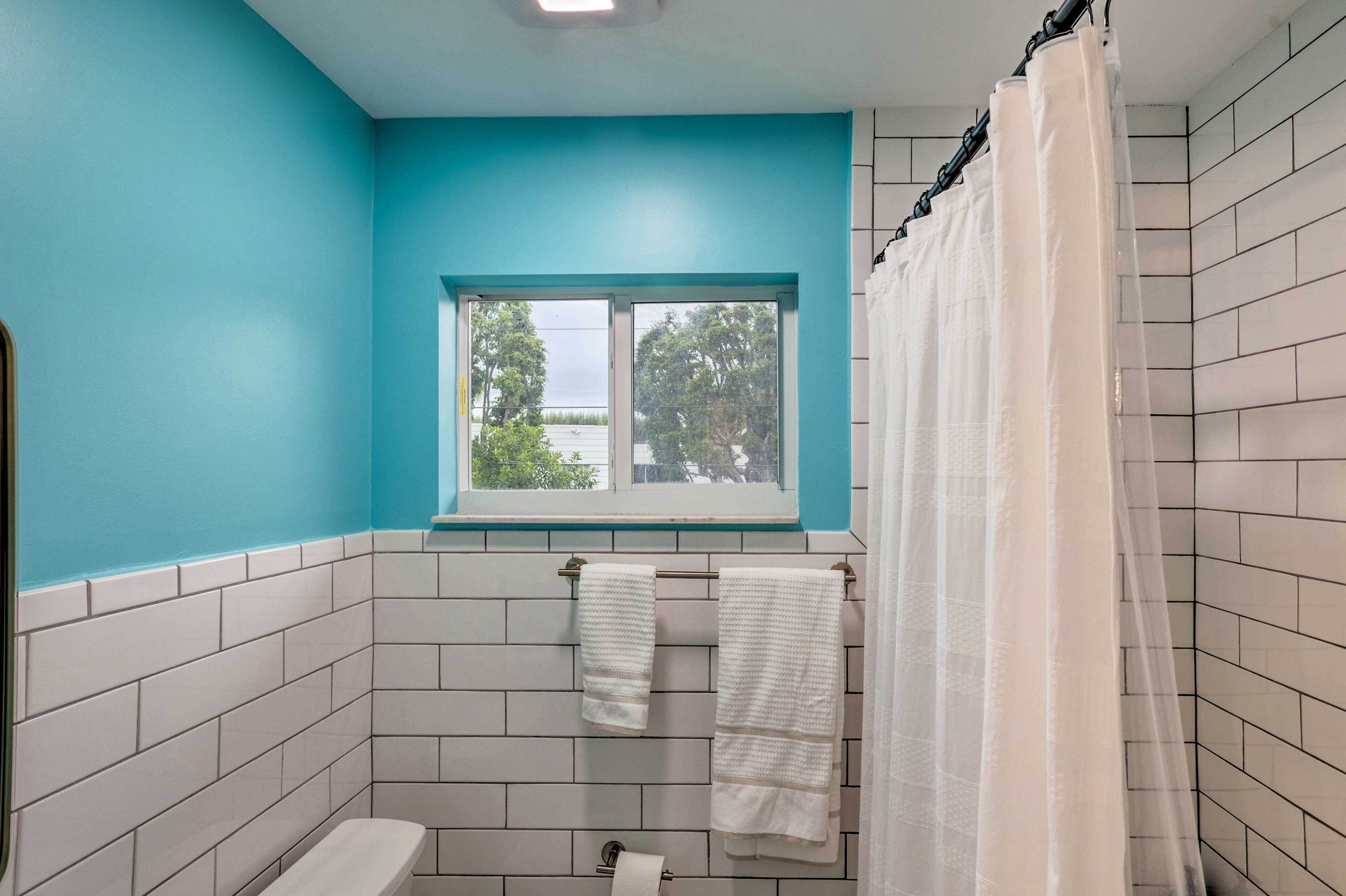 A bathroom with white tiled walls, a blue accent wall, a window with a view, and a shower curtain.
